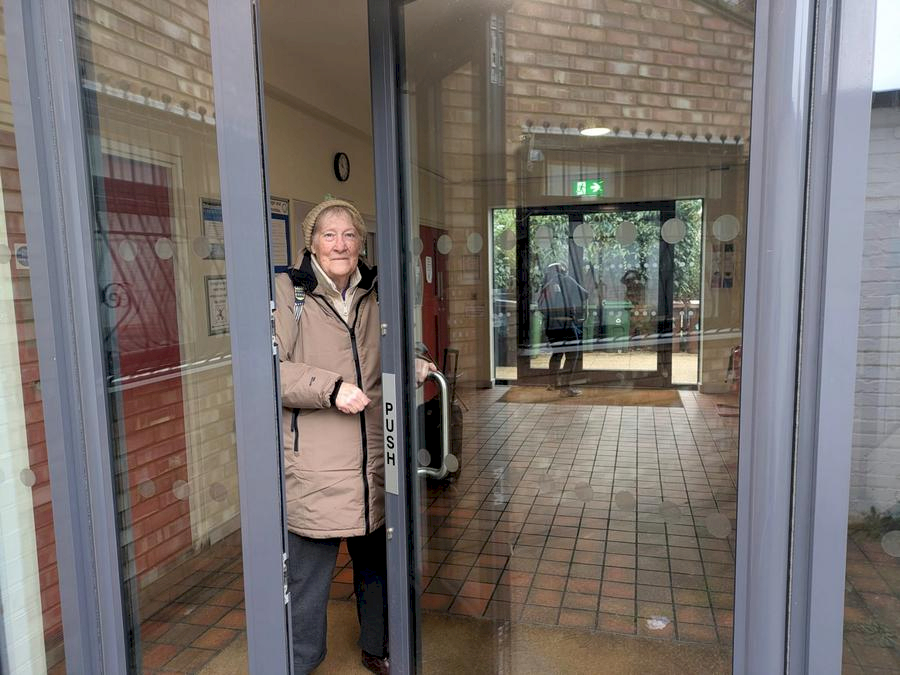 Smiling woman holding open a glass door at the building entrance