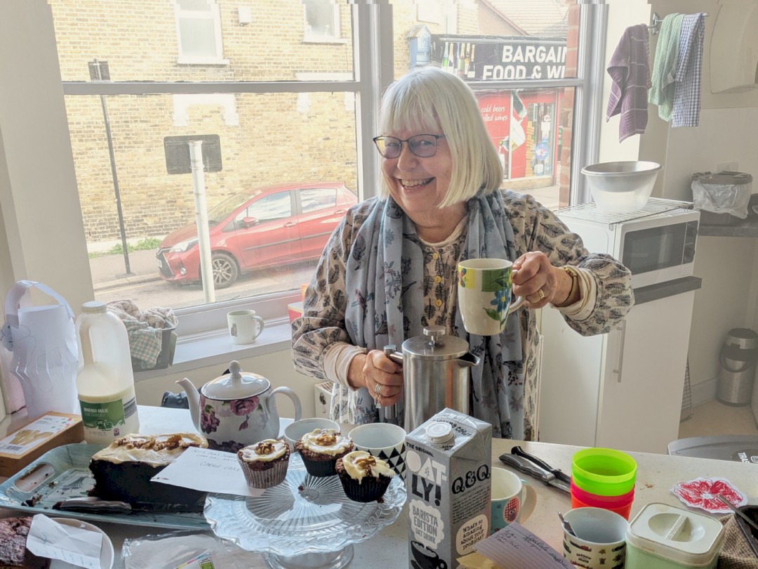 A woman holding coffee and smiling, next to some cakes A woman holding coffee and smiling, next to some cakes